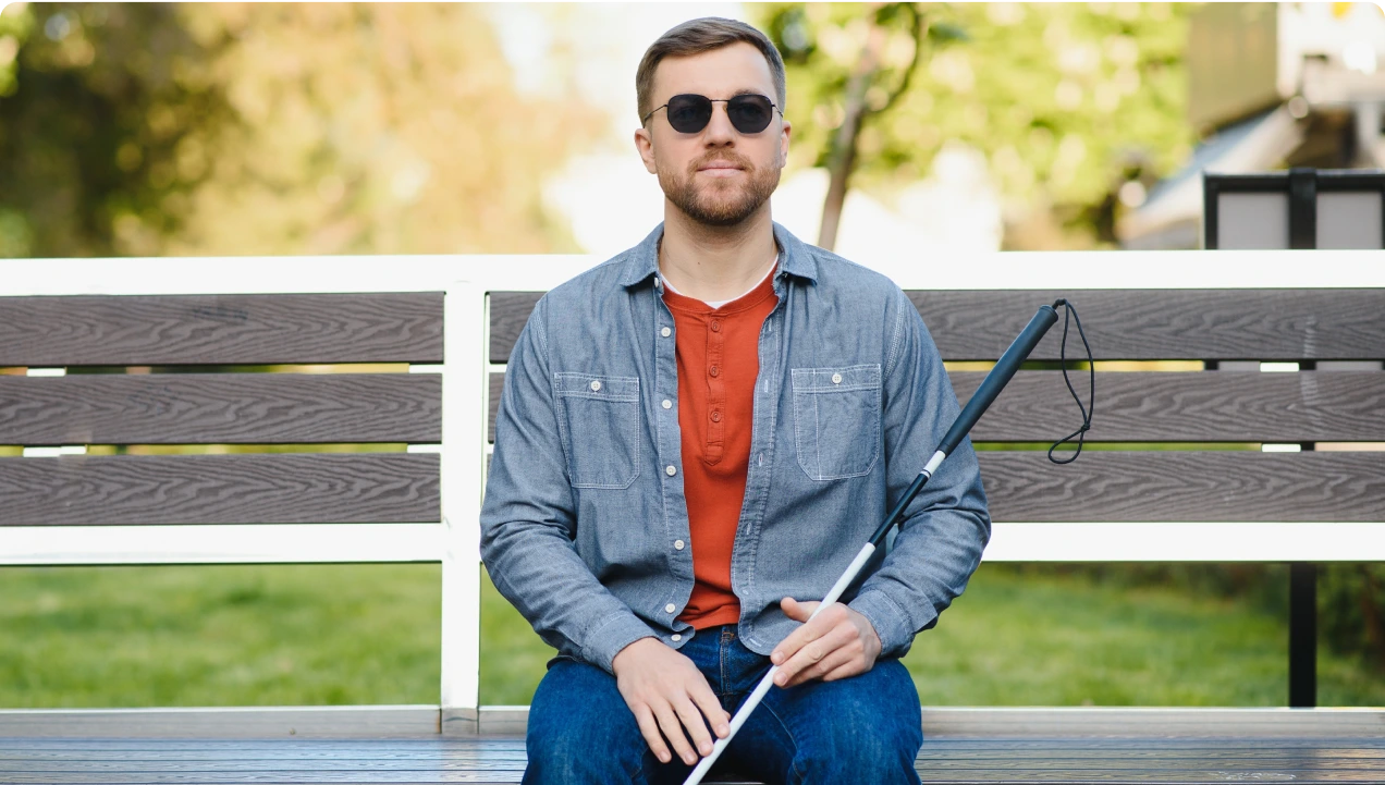 A blind man earing dark glasses sitting on a bench